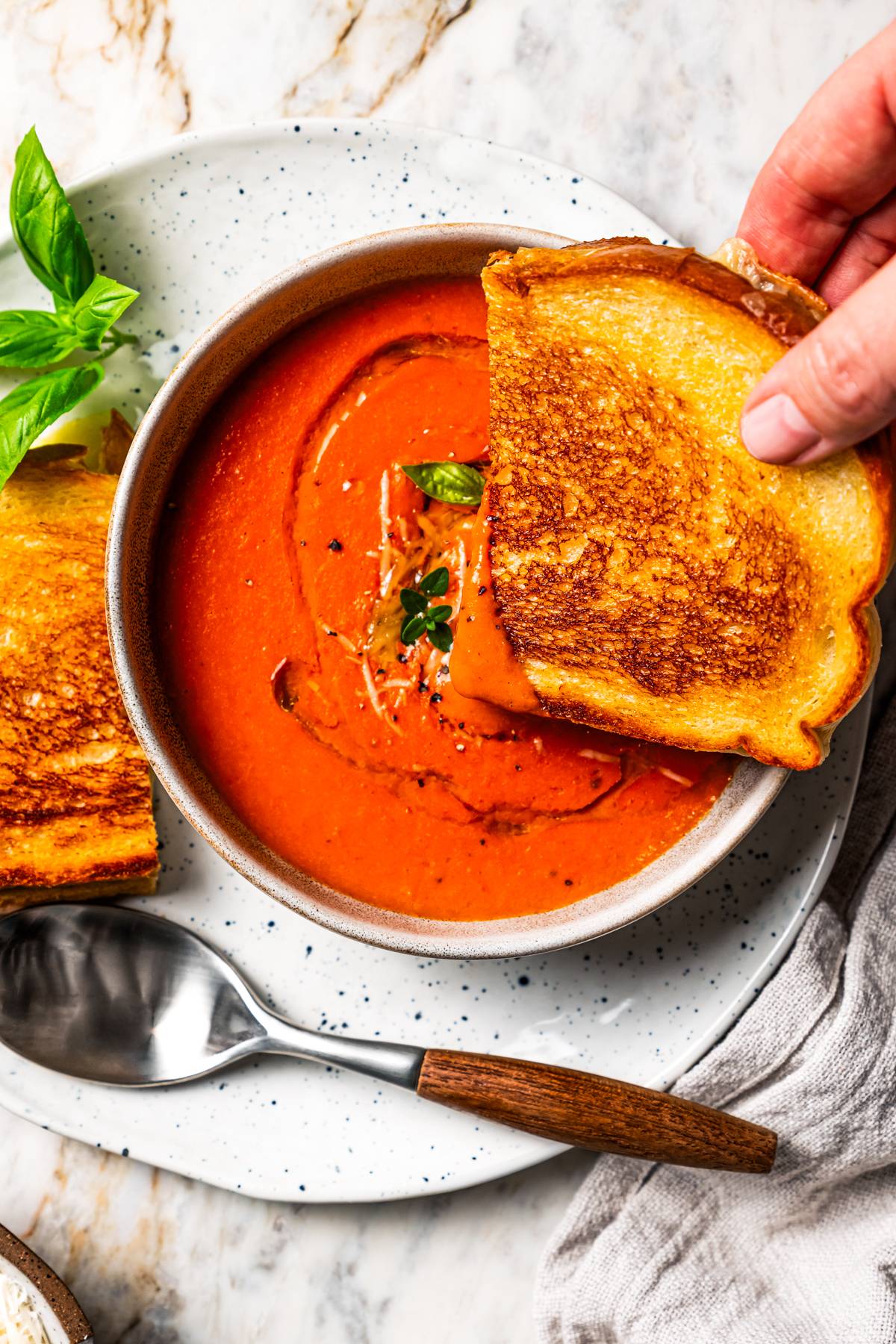 A hand dipping a grilled cheese sandwich in a bowl of tomato soup.