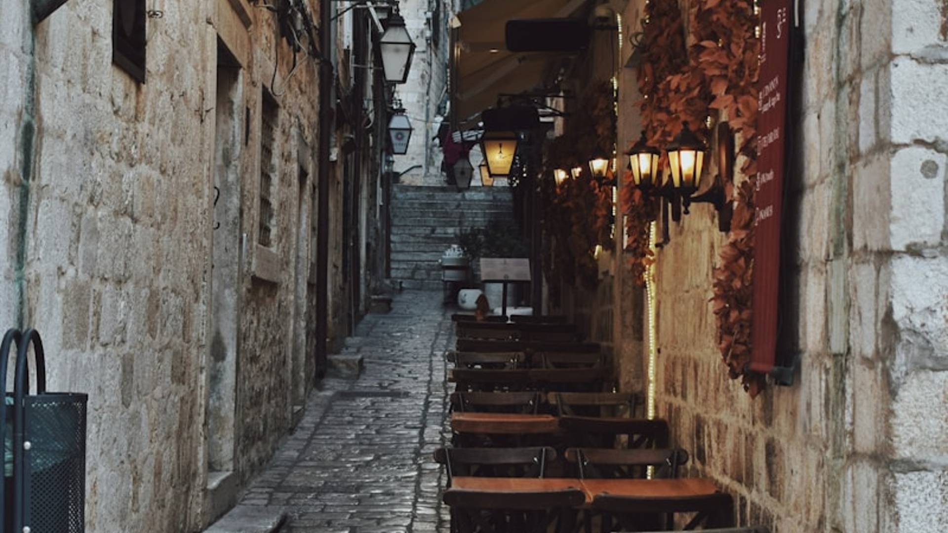 a narrow alleyway with tables and umbrellas
