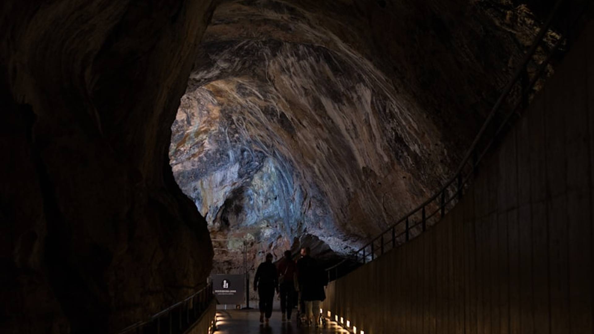 People walking through a dimly lit cave passage with lights.