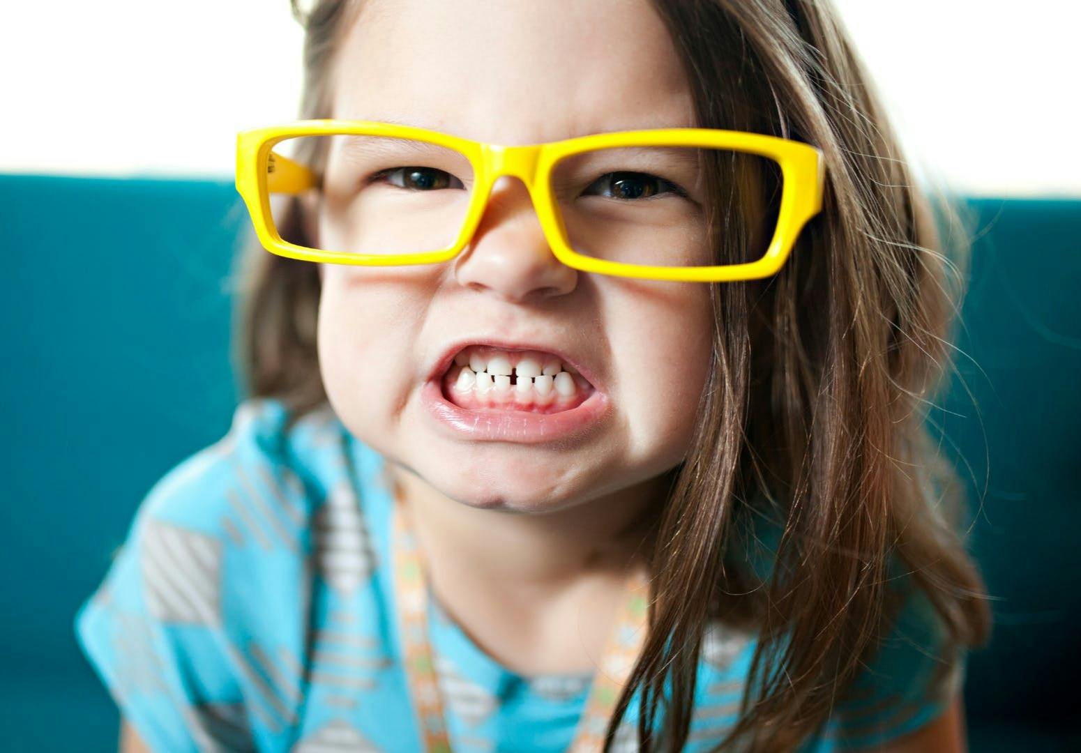 4 yr old girl with byellow glasses baring her teeth
