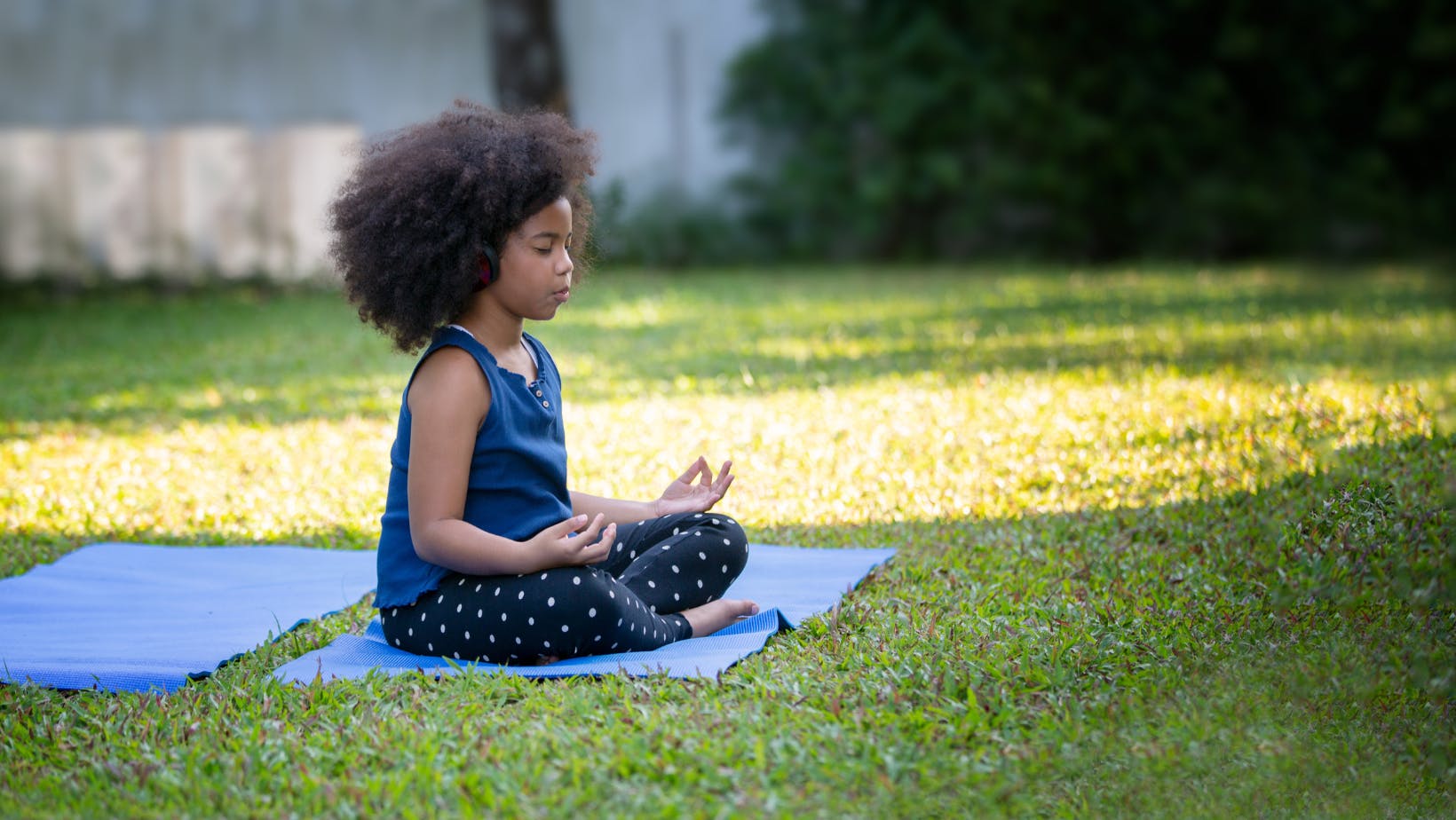african american girl sitting on mat in grass cross-legged with eyes closed