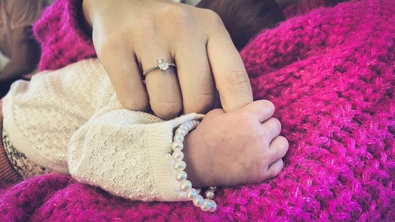 Mother holding newborn baby's hand with ring