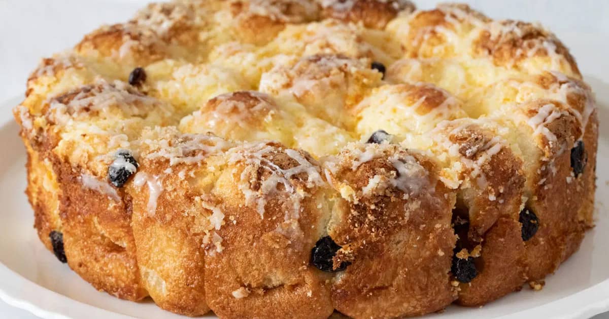 close-up of cream cheese citrus rolls, baked golden brown and crispy in a cake pan, topped with lemon icing and orange and lemon zest