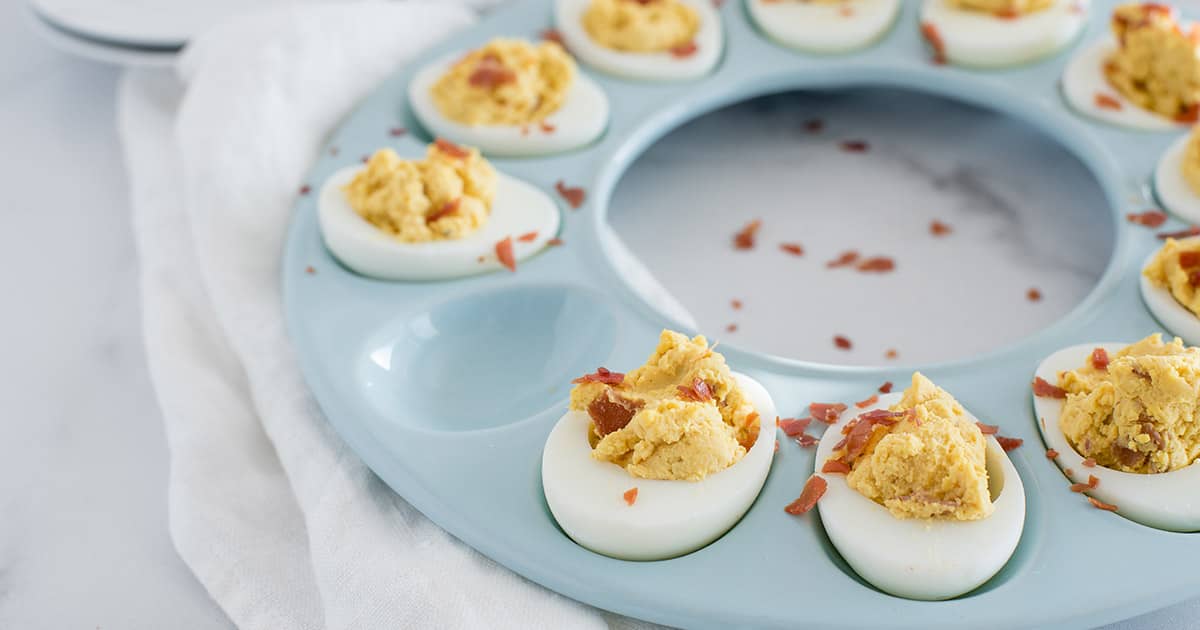 a close-up of a blue egg platter with all but one slot filled with BBQ Bacon Deviled eggs, served with the filling a little rustic and spooned in instead of piped