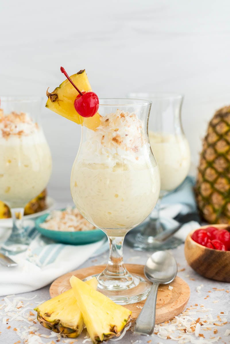 a cocktail glass filled with Instant Pot Coconut Rice Pudding, garnished with a pineapple wedge and a cherry 