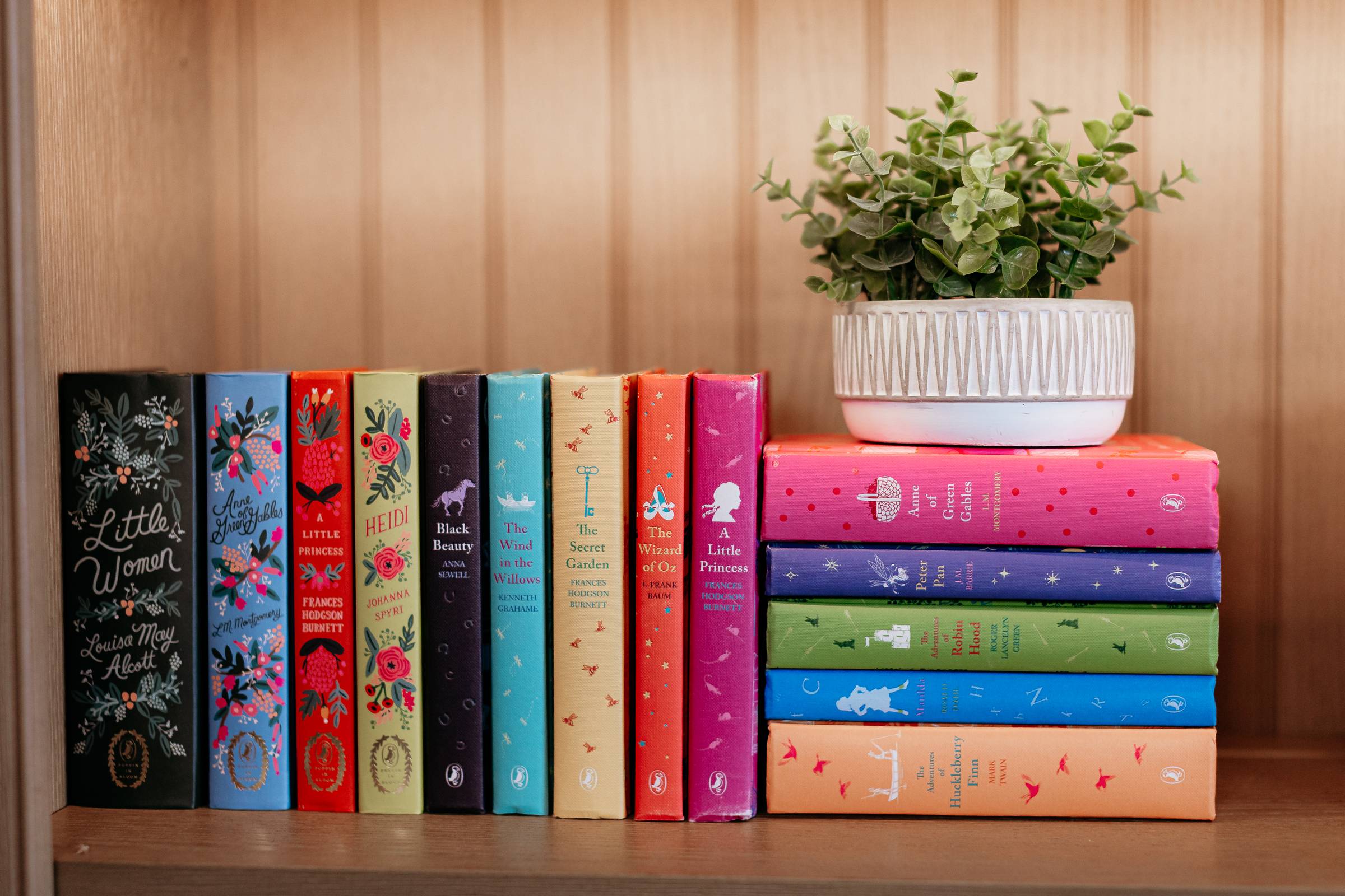 bookshelf of beautifully bound classics, with a plant on top of the stack