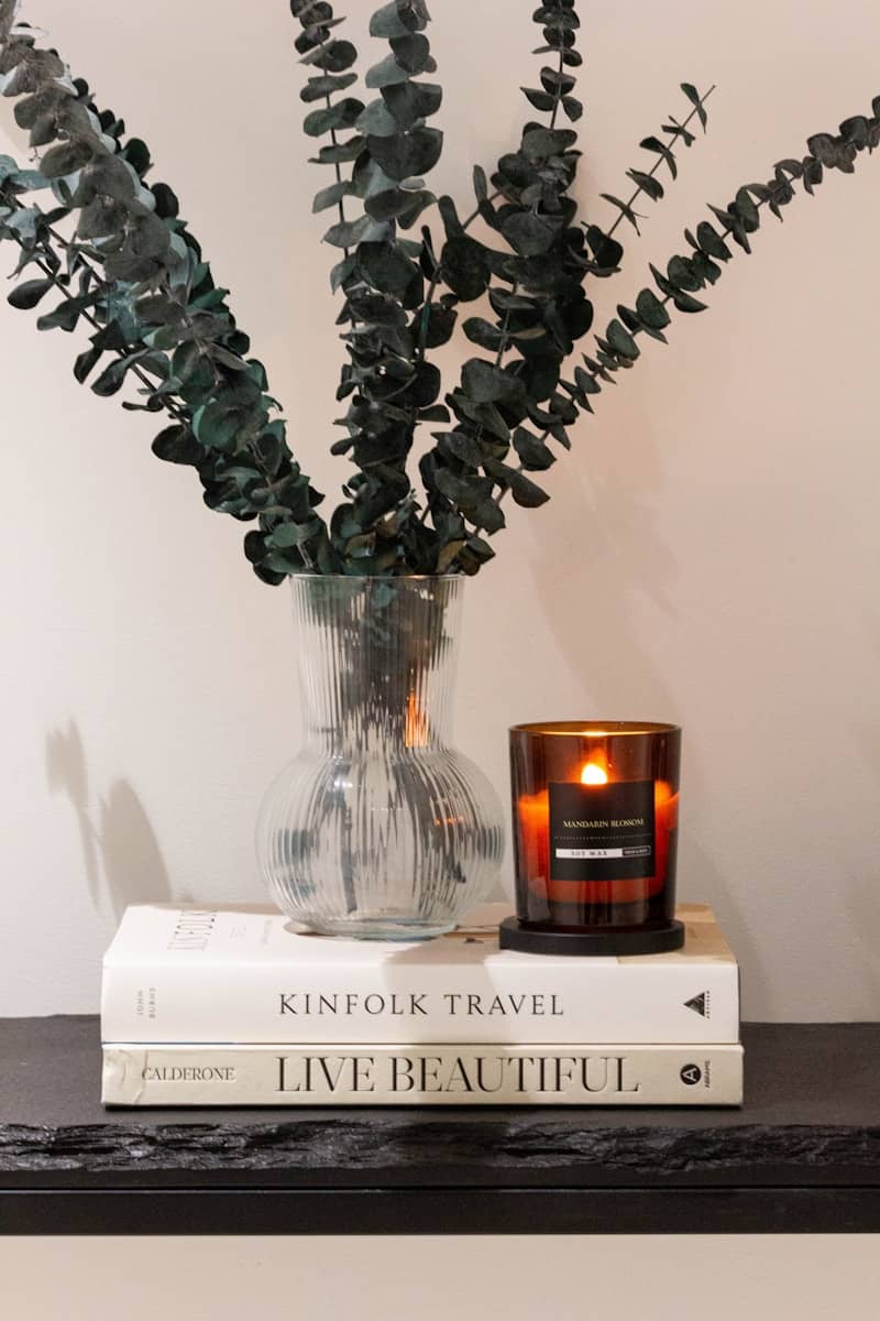 A lit candle sits on books with eucalyptus branches.