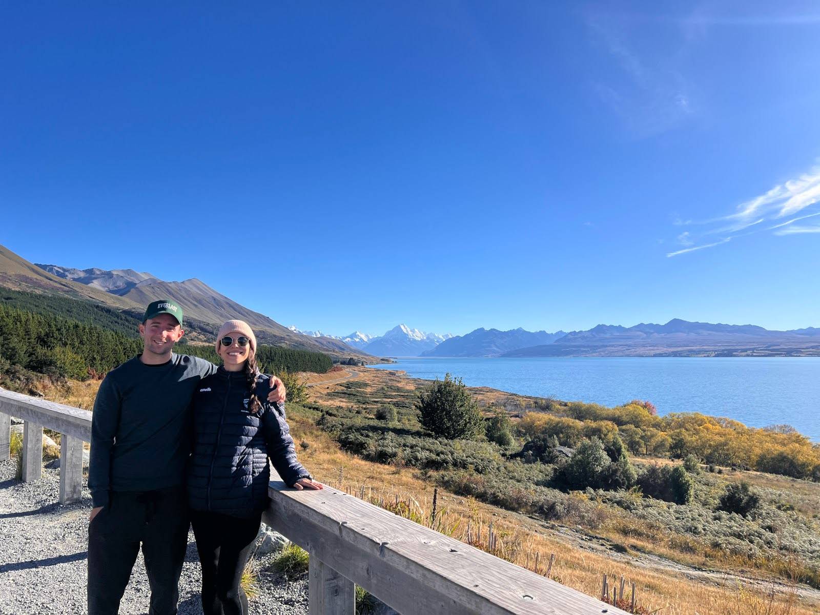 Allan and Katharina standing in front of Lake Pukaki with a mountain range in the background while traveling long-term around New Zealand with digital nomad travel health insurance.
