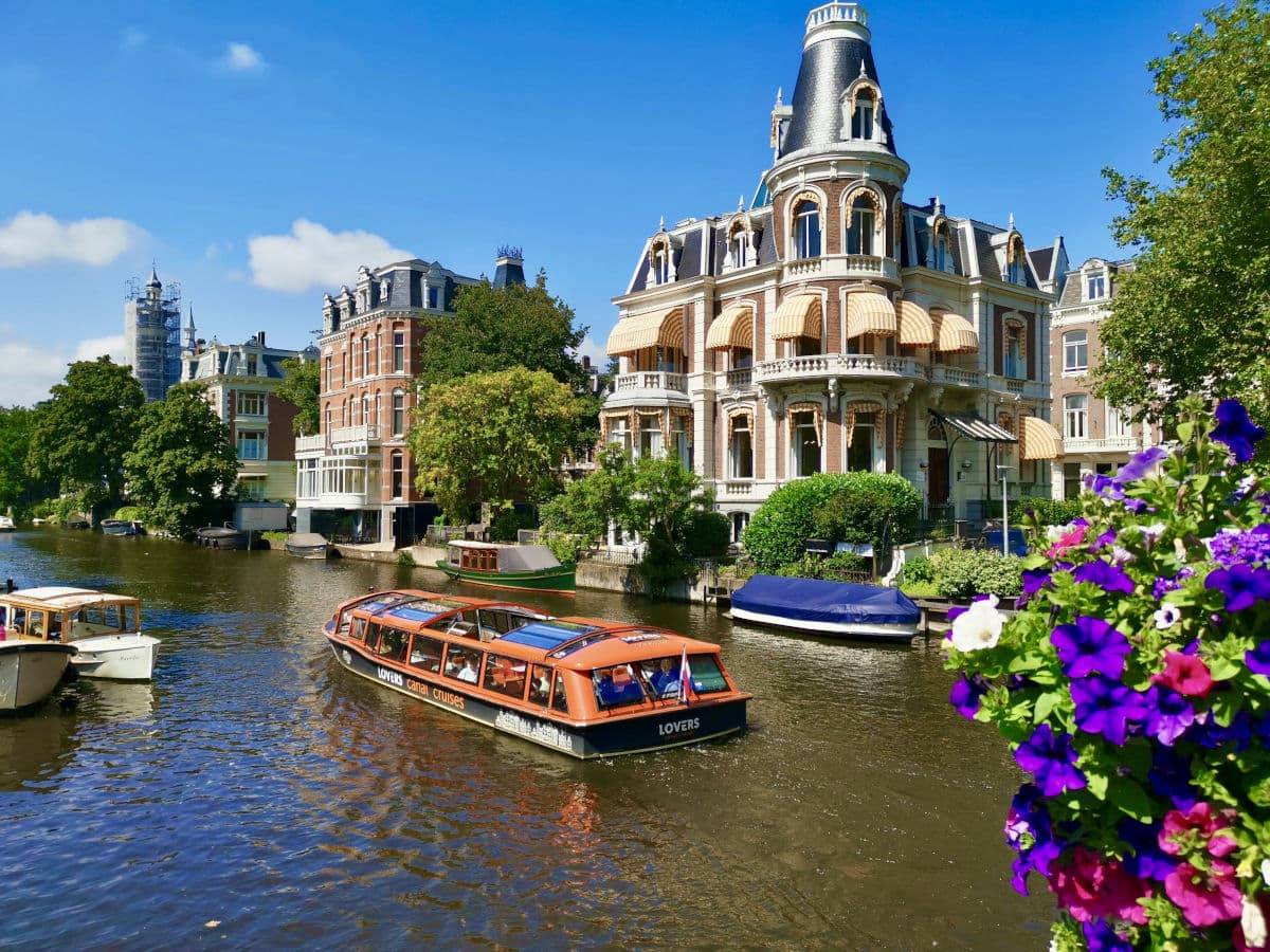 Tourists enjoy a relaxing canal boat ride past beautiful historic buildings while following their Amsterdam itinerary.