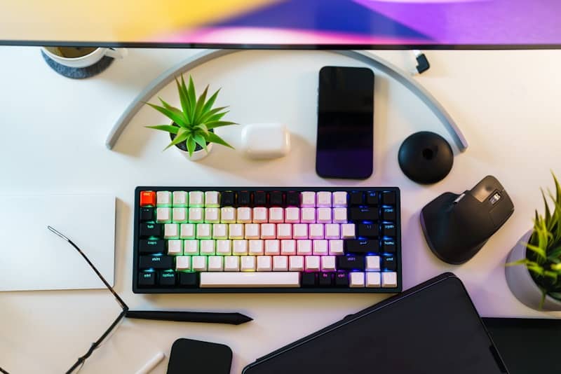 A desk with a keyboard, mouse, cell phone and a plant