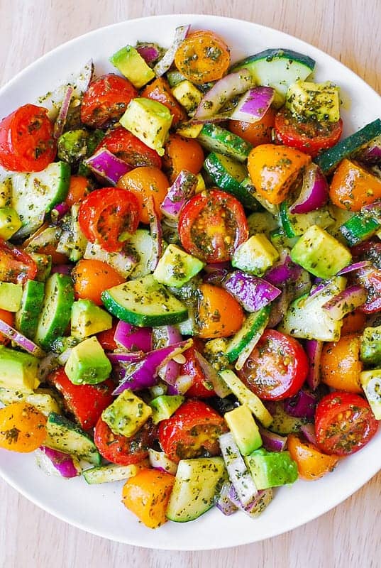 Tomato Cucumber Avocado Salad with Basil Pesto on a white plate.