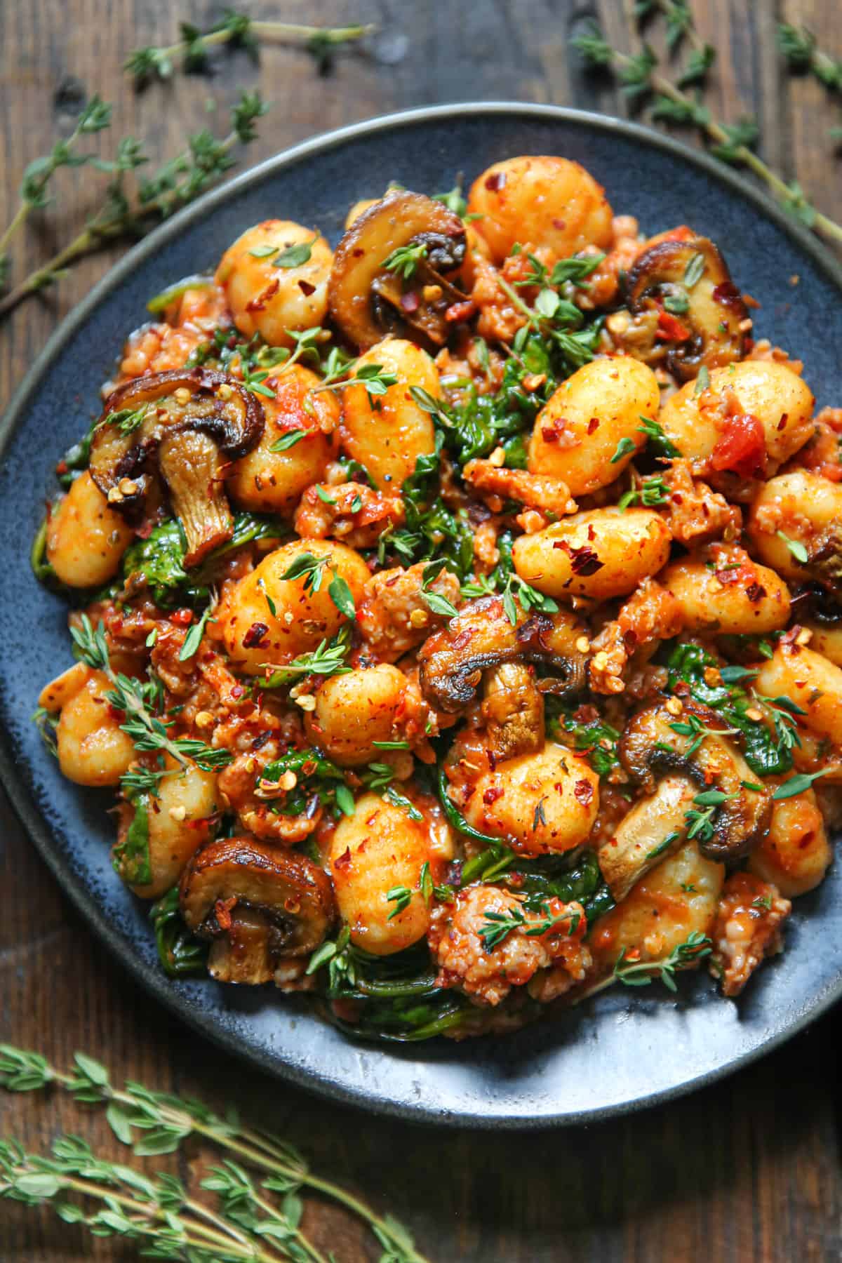 Italian Sausage Gnocchi with Spinach, Mushrooms, and Tomato Sauce on a blue plate.