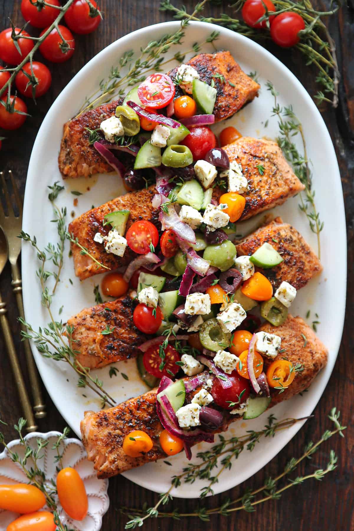 Greek Salmon with vibrant marinated veggies (kalamata olives, green olives, cherry tomatoes, cucumber, red onion) and feta cheese mixture on a white plate.