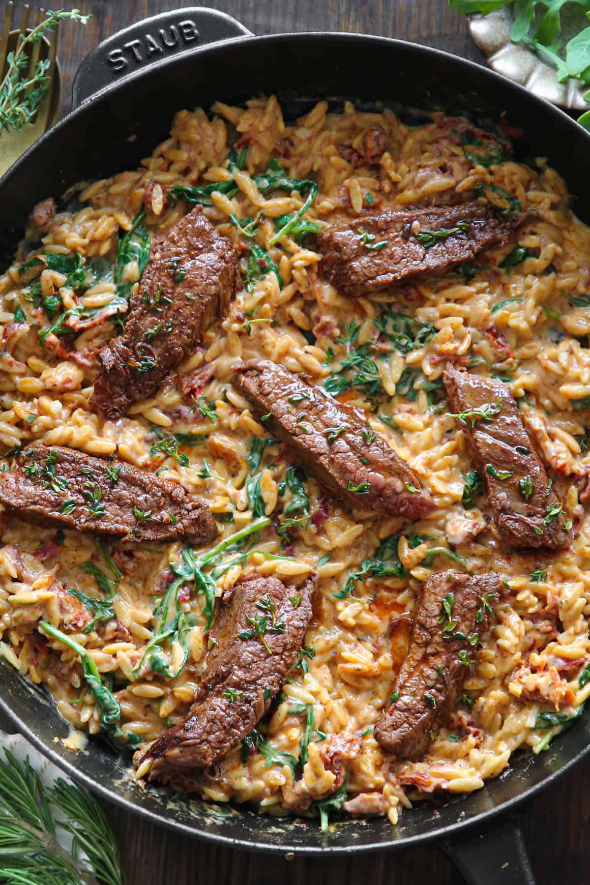 Sliced Steak with Creamy Spinach and Sun-Dried Tomato Orzo in a cast iron skillet.