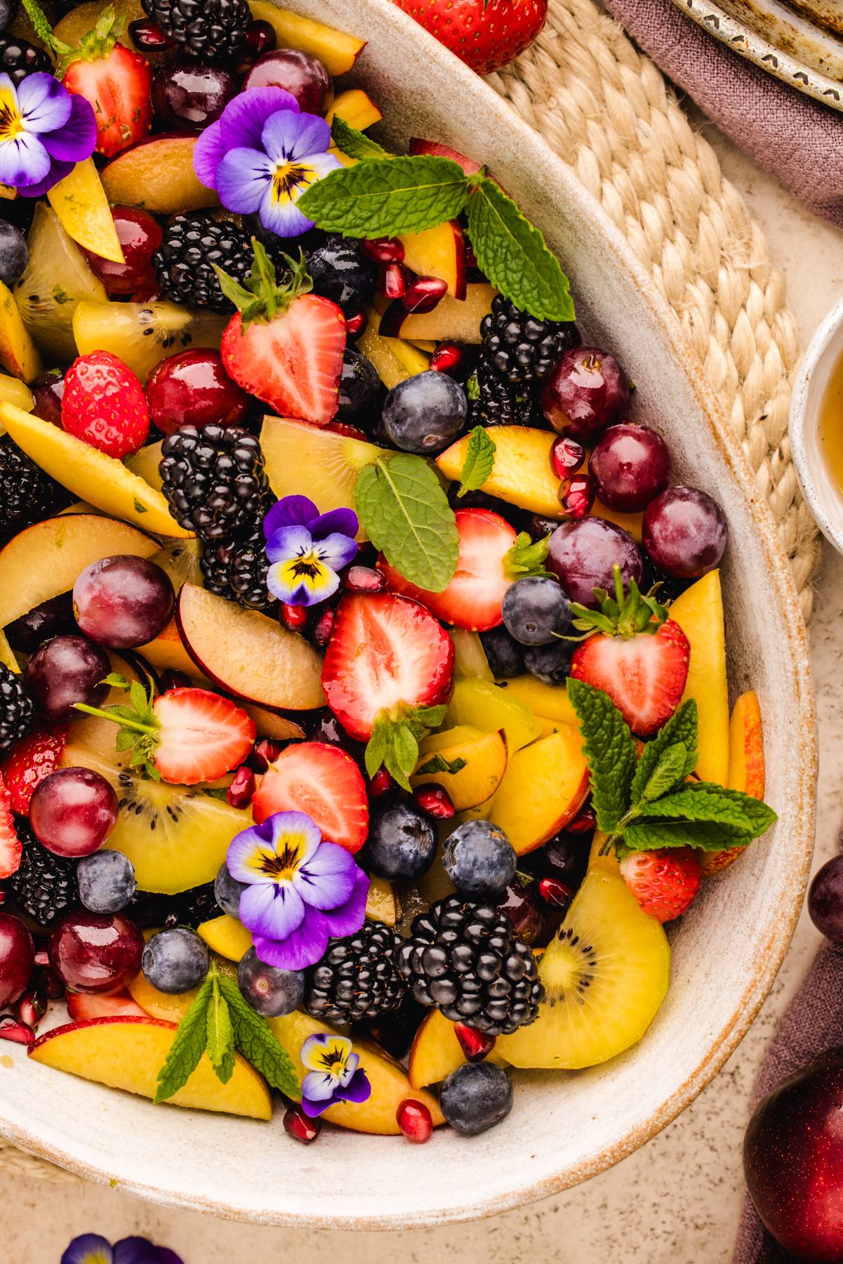 Summer Fruit Salad (with strawberries, nectarines, peaches, plums, kiwi fruit, blueberries, grapes, blackberries, and pomegranate seeds) on a white plate.