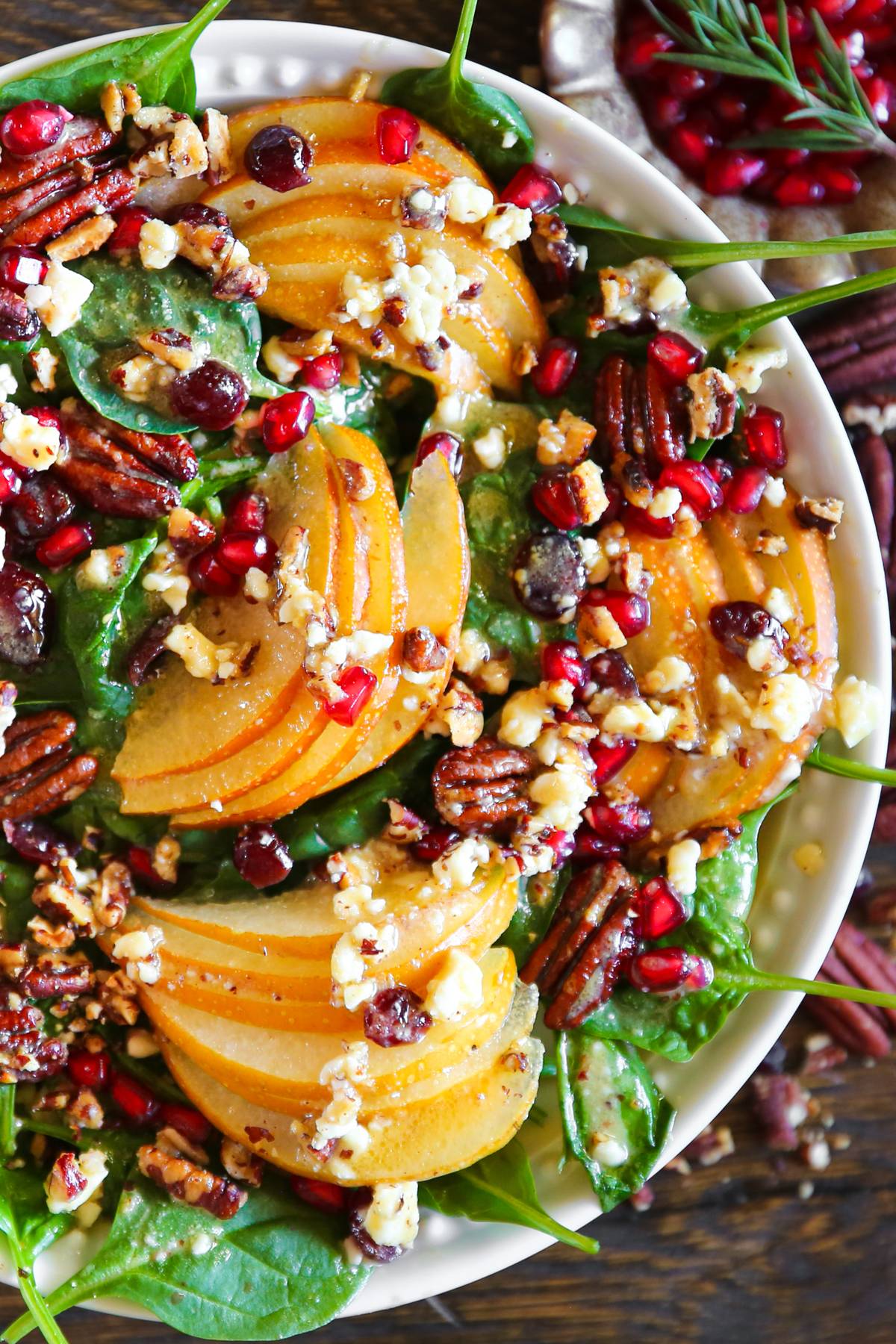 Pear and Pomegranate Spinach Salad with Maple-Lemon Mustard Dressing in a white bowl.