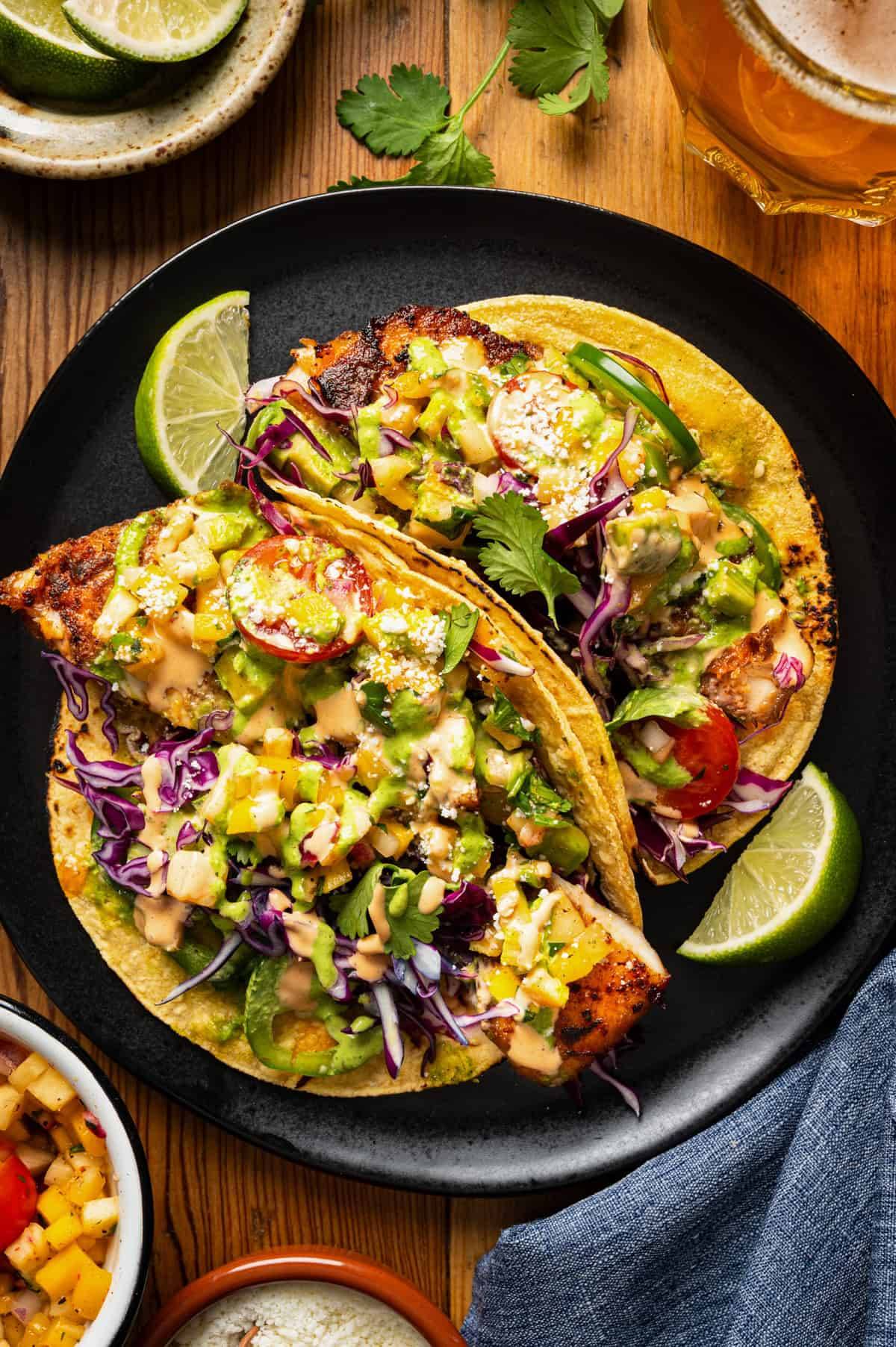 Fish Tacos with Avocado, Cotija, and Pineapple-Mango Salsa on a black plate.