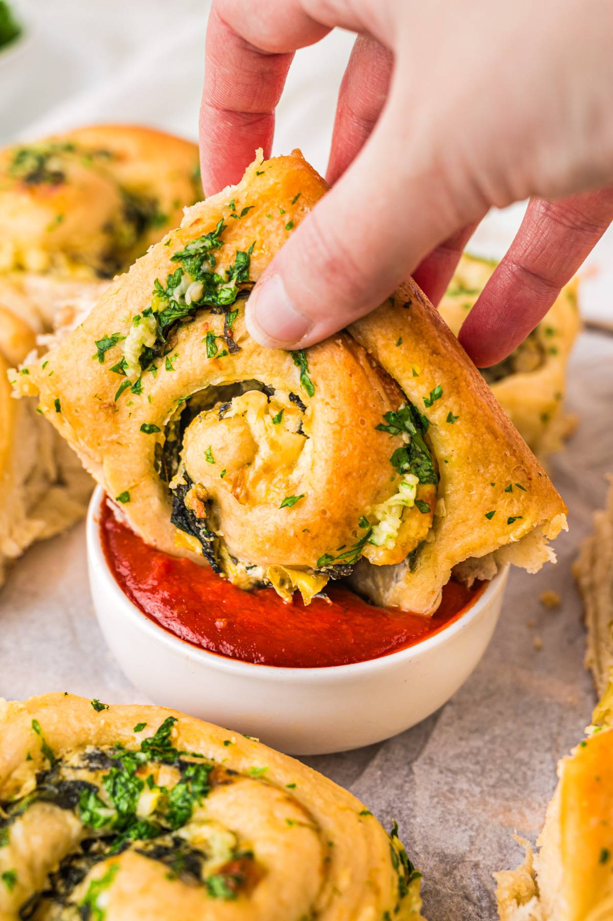 Dipping spinach-artichoke bun into the bowl with red sauce.