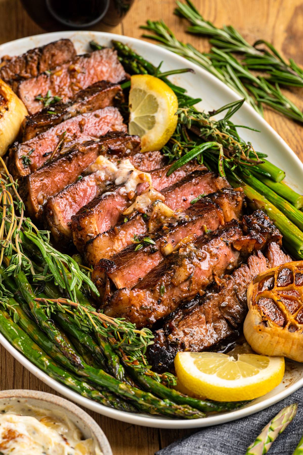 Pan-Seared Marinated Ribeye Steak with Roasted Garlic, Asparagus on a platter.