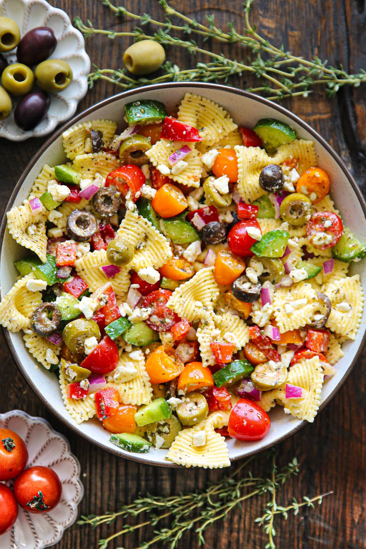 Greek Pasta Salad with tomatoes, cucumber, olives, feta cheese - in a white bowl.