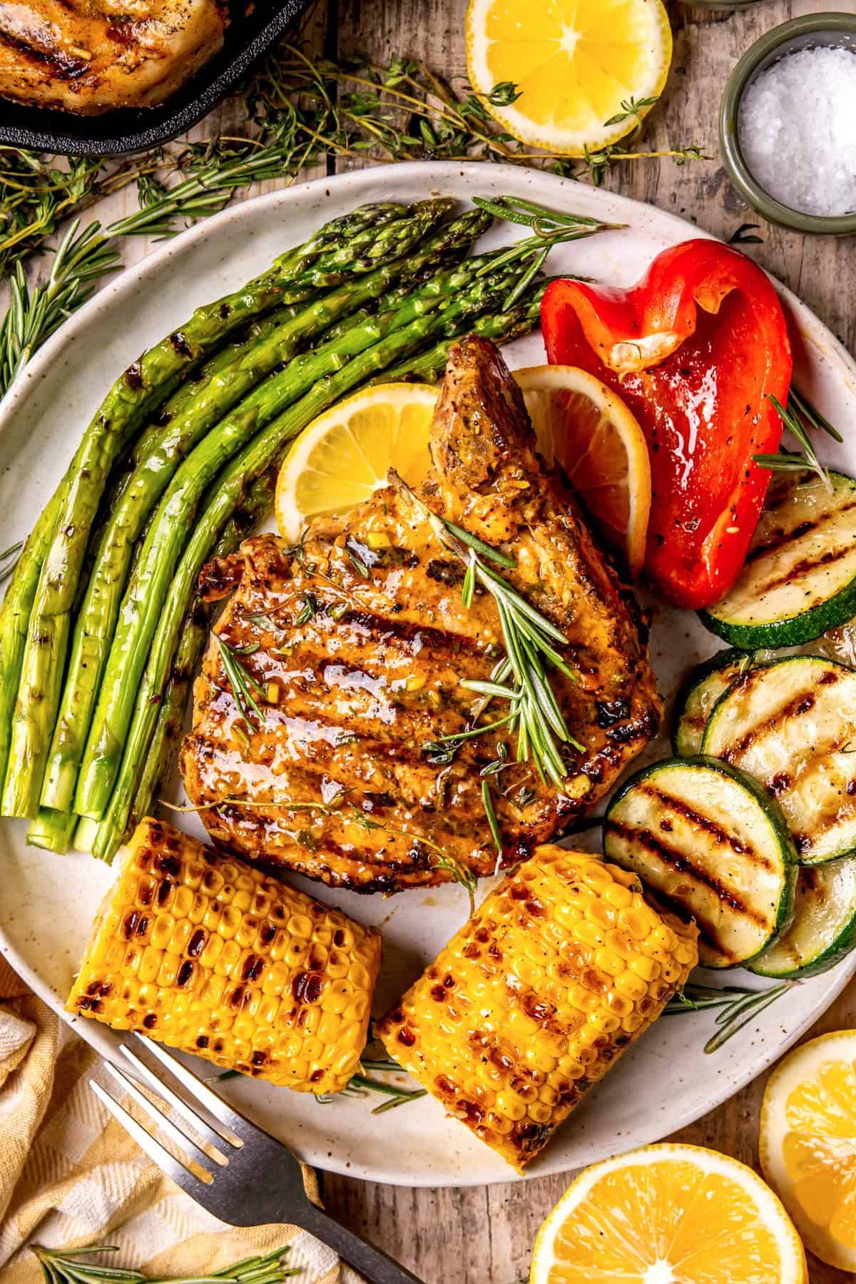 Grilled Pork Chops? with Dijon-Honey Herb Marinade and grilled veggies (asparagus, bell peppers, zucchini, and corn) - on a plate.