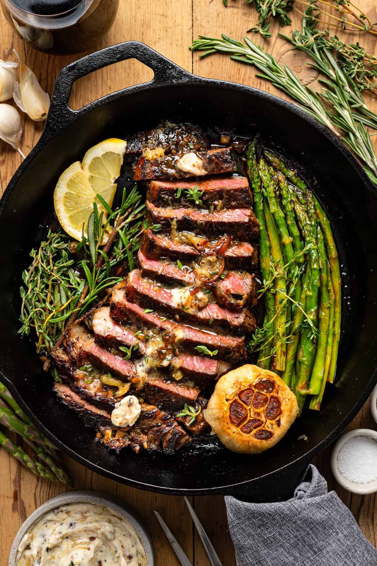 Marinated Ribeye Steak with Roasted Garlic Butter & Asparagus in a cast iron pan.