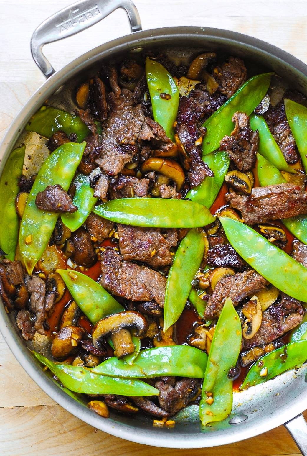 Asian Beef with Mushrooms and Snow Peas in a stainless steel pan.