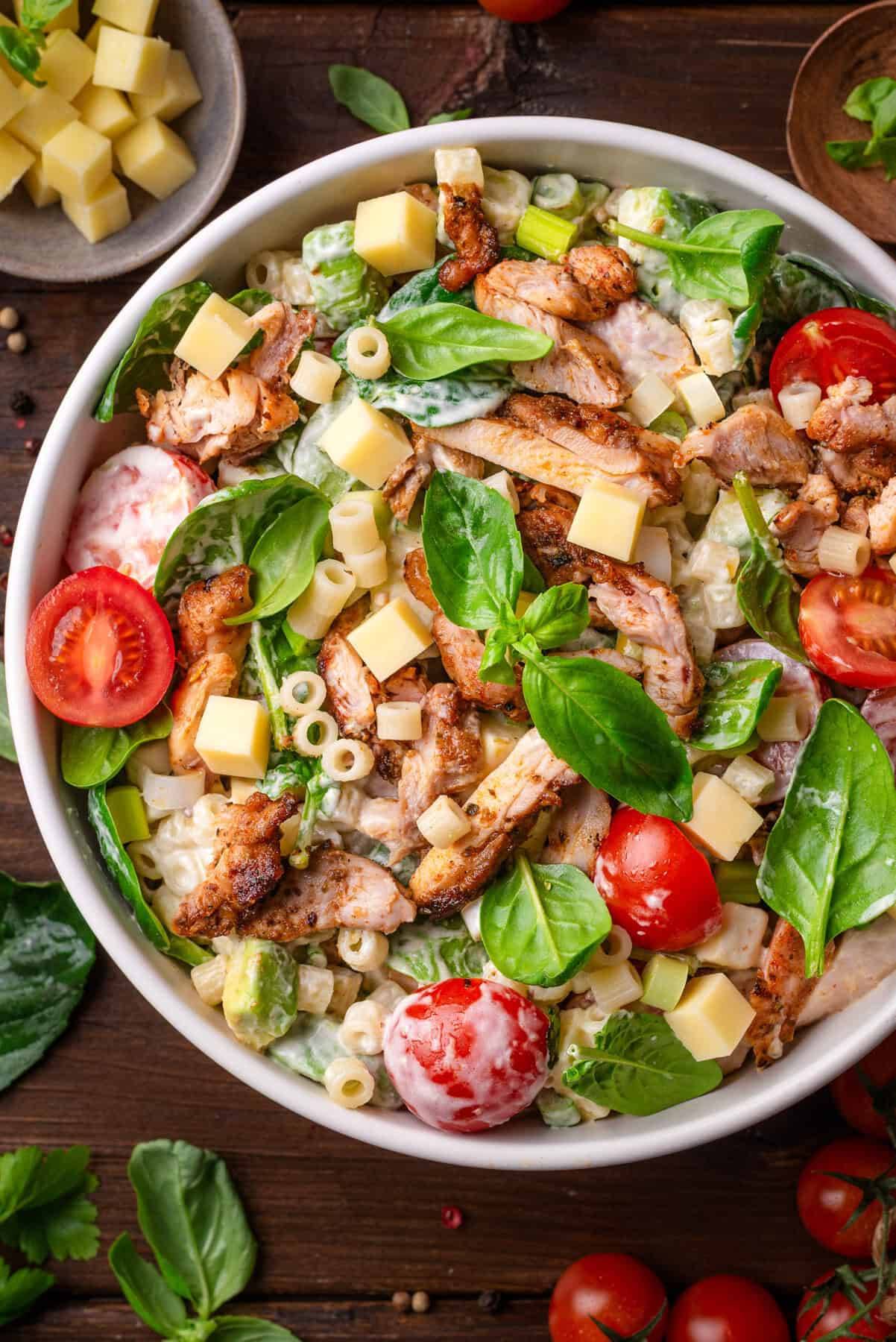 Creamy Chicken Pasta Salad (with cherry tomatoes, spinach, avocado, sharp cheddar, and a tangy yogurt-mayo dressing) in a bowl.
