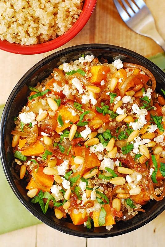 Quinoa Salad with Roasted Butternut Squash, Pine Nuts, Caramelized Onions, and Feta cheese in a black bowl.