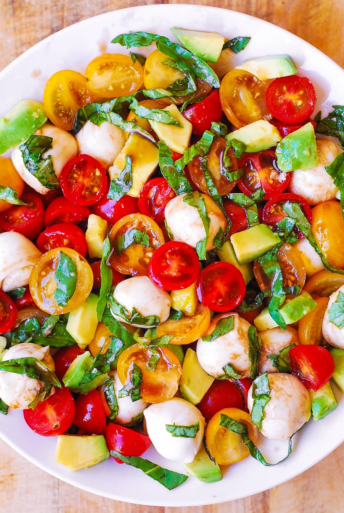 Tomato Basil Avocado Mozzarella Salad with Balsamic Dressing on a white plate.