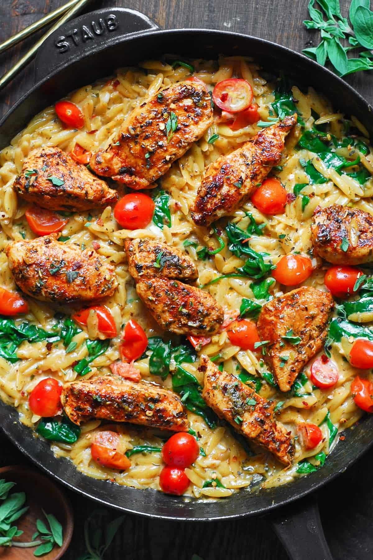 Creamy Chicken Orzo with Cherry Tomatoes, Spinach, and Basil Pesto Sauce - in a cast iron skillet.