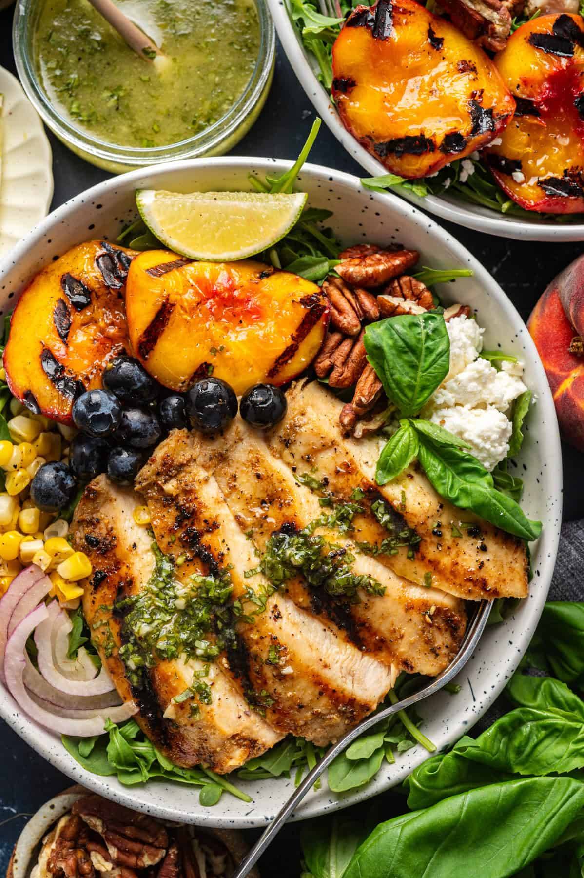 Chicken and Peach Salad on top of Spinach with Honey-Mustard Basil Dressing in a white bowl.