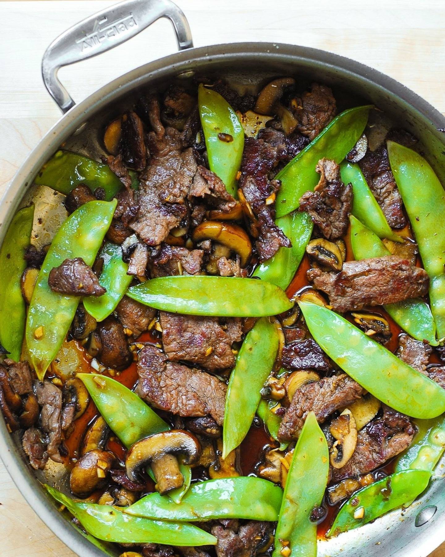 Asian Beef with Mushrooms and Snow Peas in a stainless steel pan.