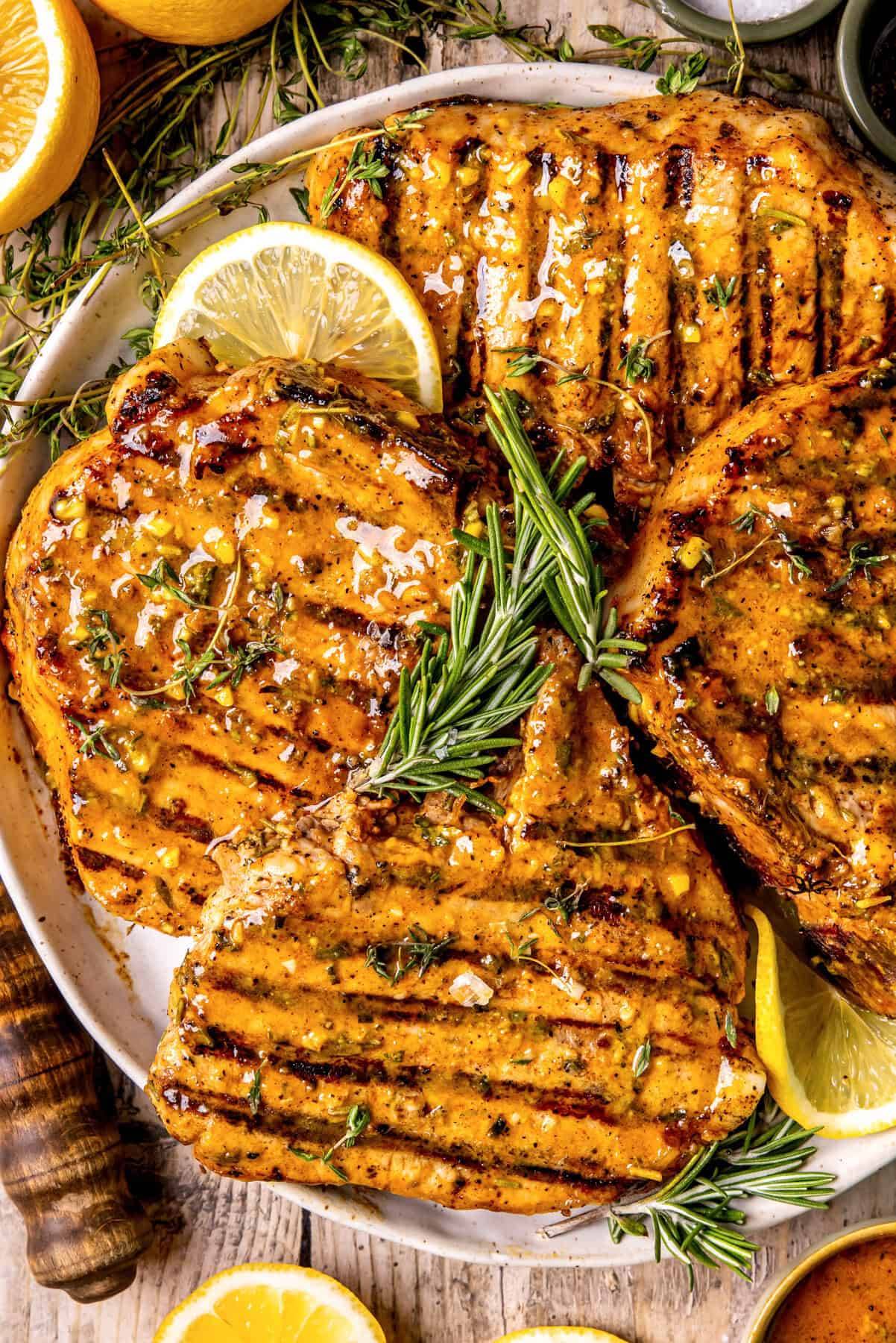 Grilled Pork Chops with lemon and fresh herbs on a white plate.