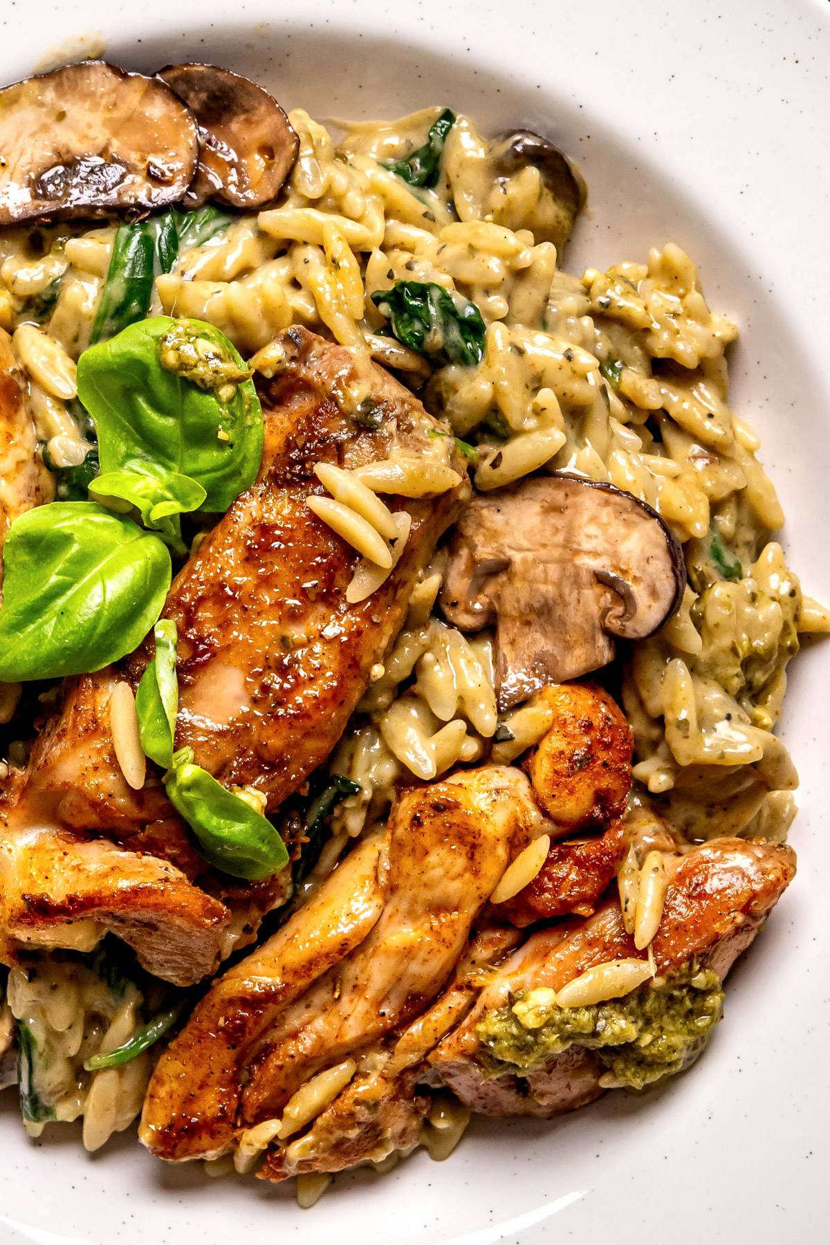 One-Pan Creamy Chicken Orzo with Mushrooms, Spinach, and Basil Pesto - on a white plate.
