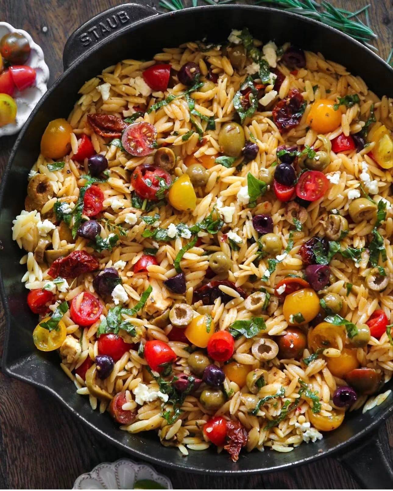 Greek Orzo with Cherry Tomatoes, Olives, and Feta cheese in a cast iron skillet.