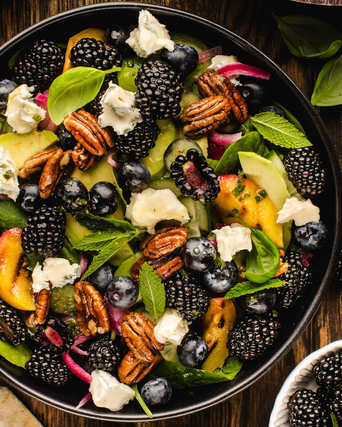 Summer Spinach Salad with Blackberries, Peaches, Avocado, Dijon-Honey-Lemon Dressing in a black bowl.