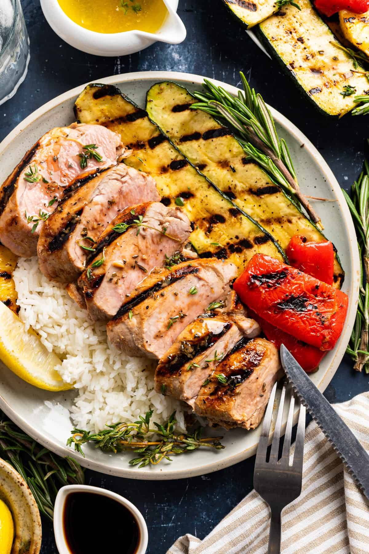 Marinated Grilled Pork Tenderloin with Caramelized Pineapple, Grilled Veggies, and Garlic Herb Butter and Rice - on a white plate.