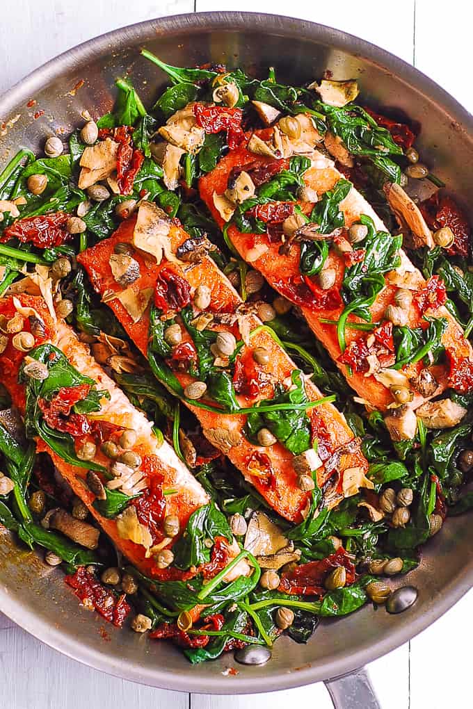 Pan-Seared Salmon with Spinach, Artichokes, and Sun-Dried Tomatoes in a stainless steel pan.