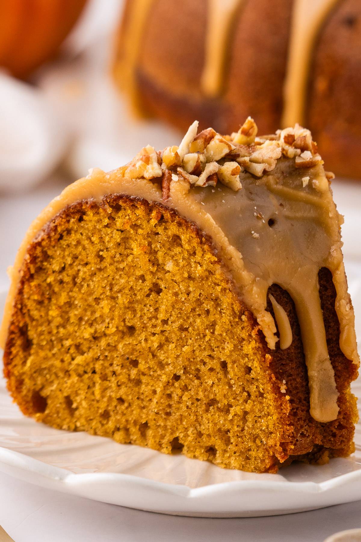 A slice of Pumpkin Bundt Cake with Brown Sugar Glaze & Pecans on a plate.