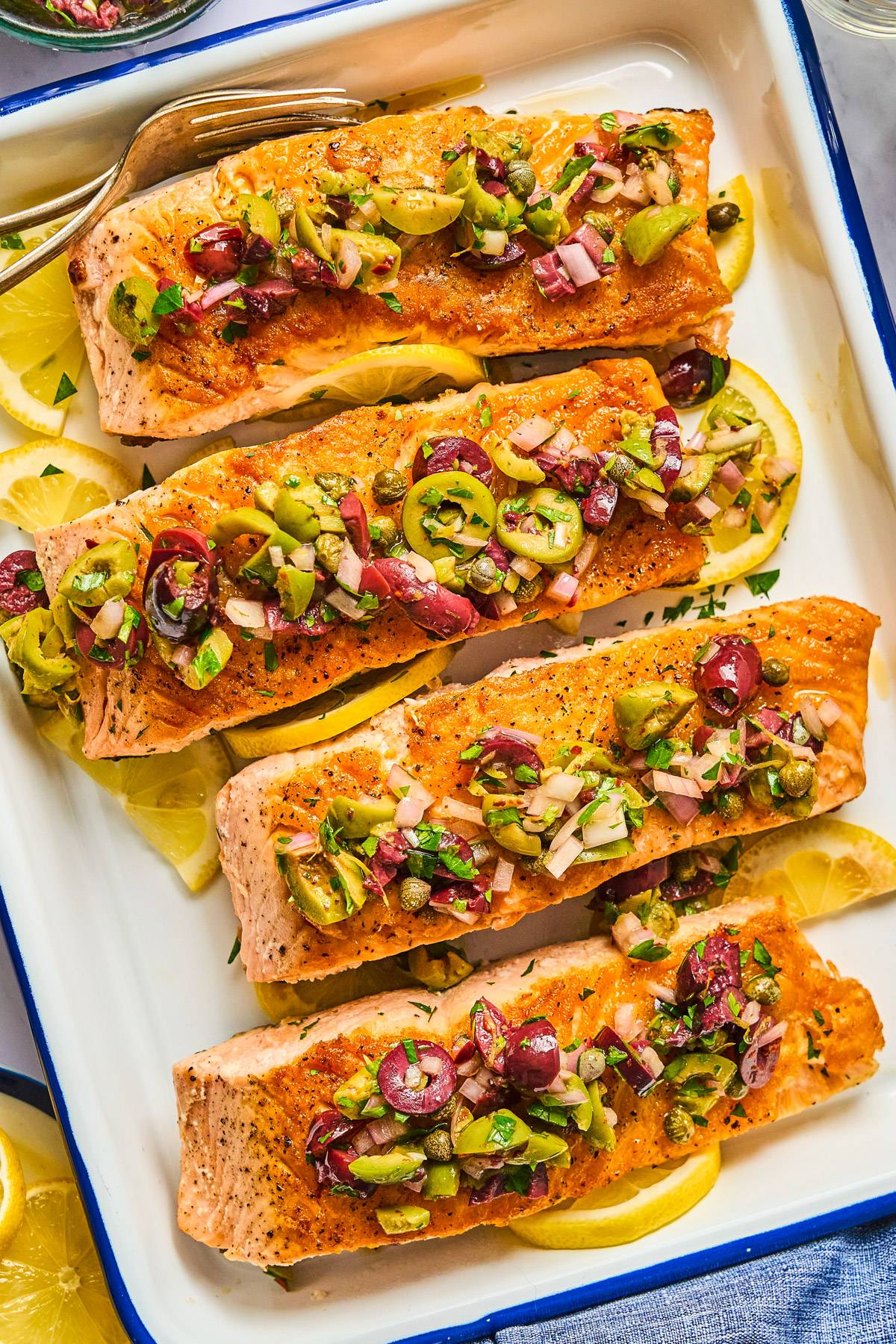 Salmon Fillets topped with chopped olives and capers in a white baking dish.