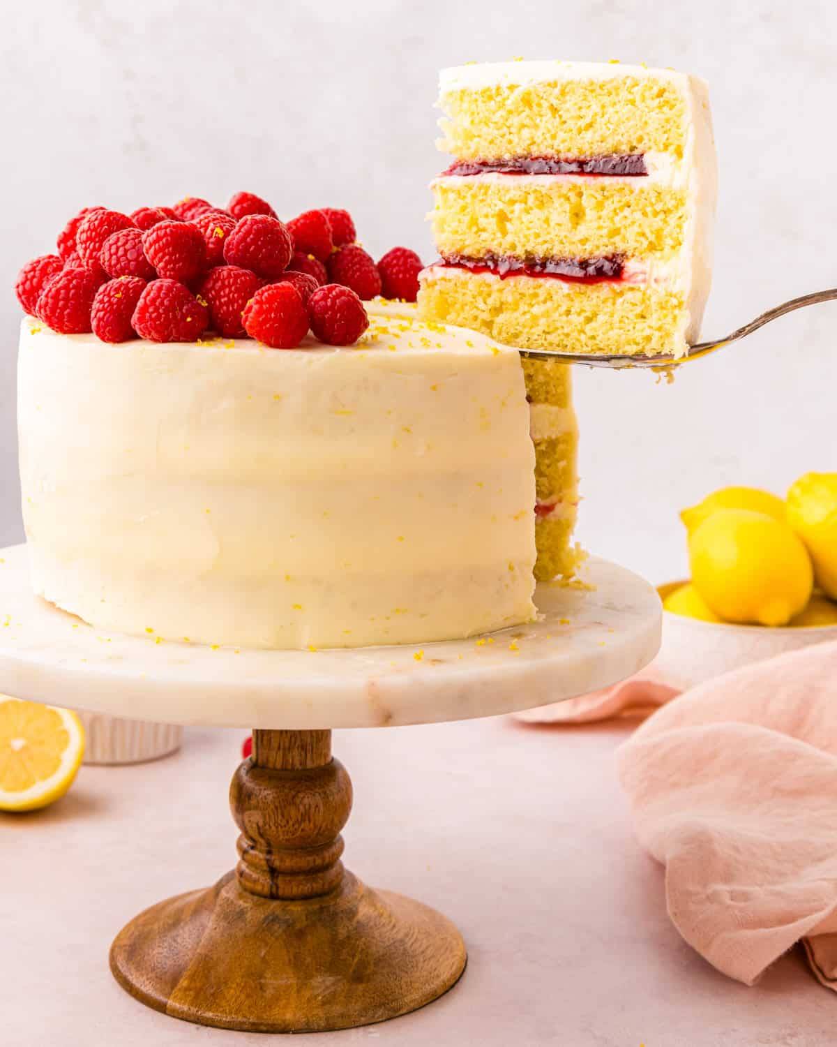 A whole lemon raspberry cake with a slice taken out (and shown) on a spatula.