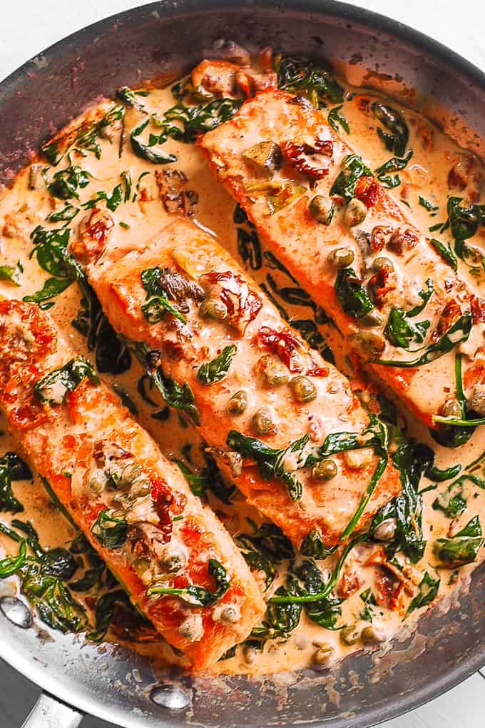 Creamy Tuscan Salmon with Garlic, Spinach, Artichokes, Sun-Dried Tomatoes, and Capers in a stainless steel pan.