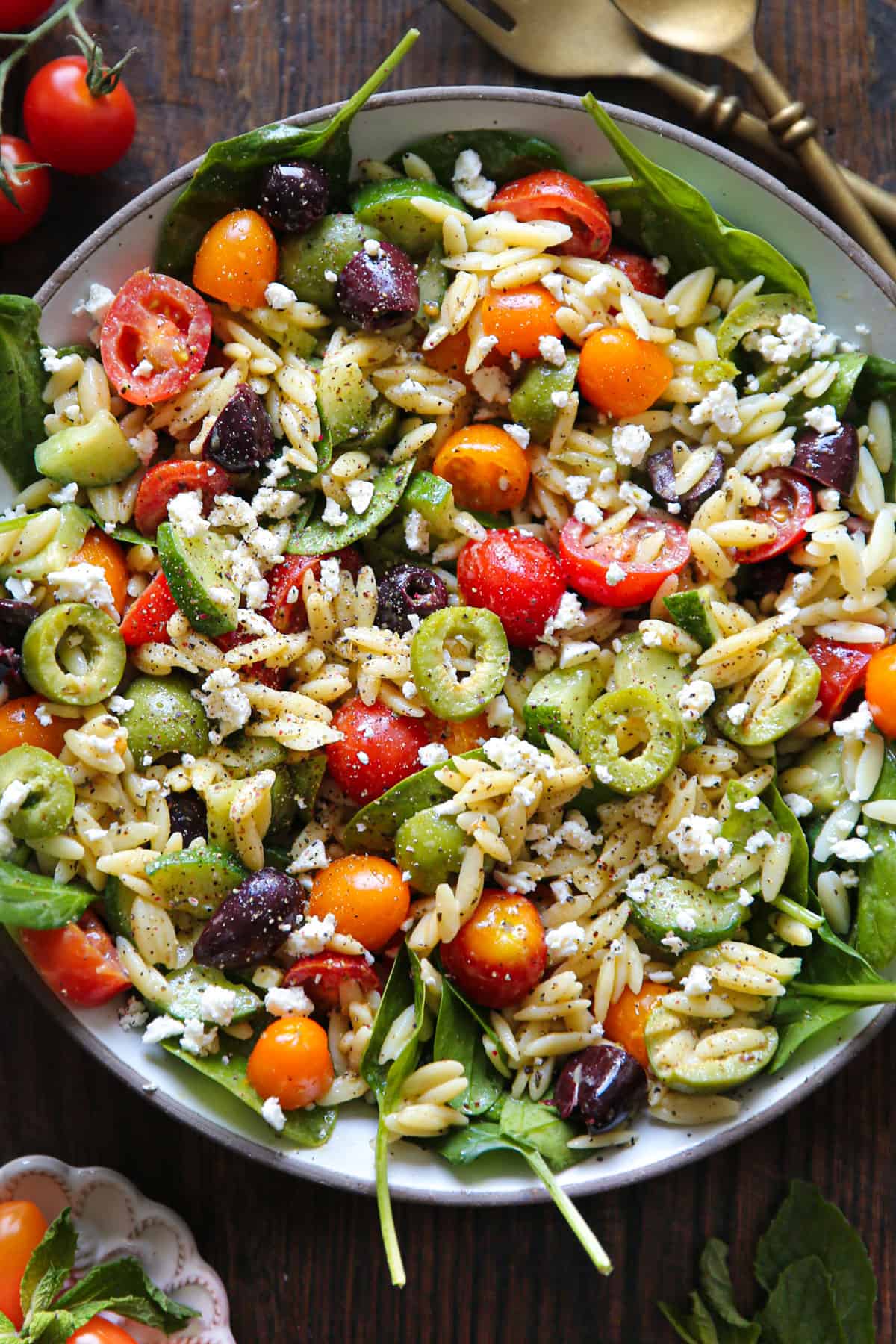 Italian Orzo Salad with spinach, tomatoes, feta, cucumber, olives - in a white bowl.