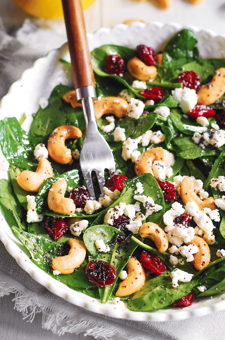 Cranberry Spinach Salad with Cashews and Goat Cheese and Lemon-Honey Poppy Seed Dressing - in a white bowl.