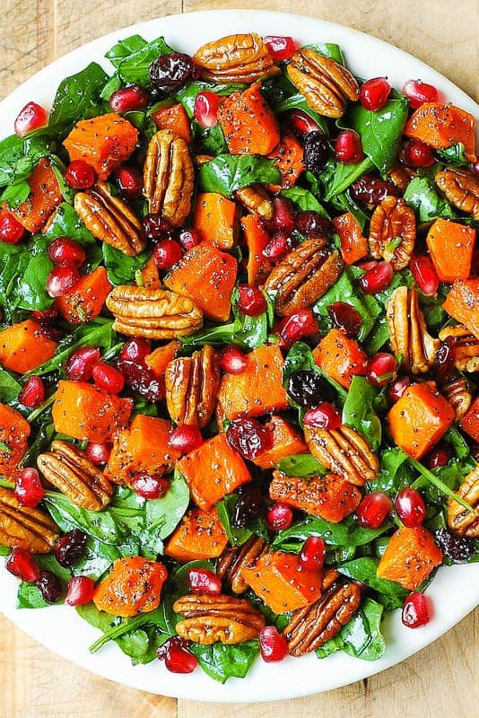 Butternut Squash and Spinach Salad with Pecans, Cranberries, Pomegranate Seeds, and Poppy Seed Honey-Lime Dressing on a white plate.