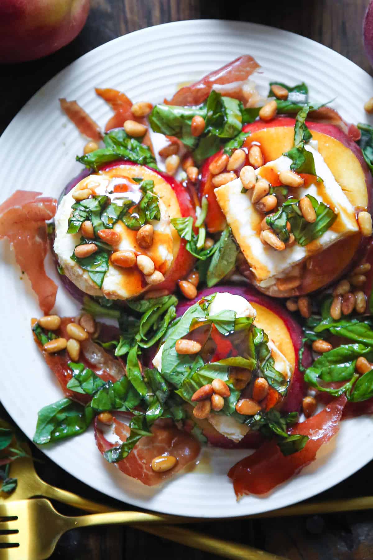 Peach Mozzarella Salad with Basil, Pine Nuts, Prosciutto, and Balsamic Dressing on a plate.
