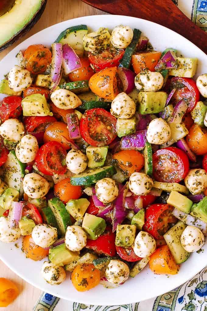 Tomato Cucumber Avocado Salad with Mozzarella and Basil Pesto on a plate.