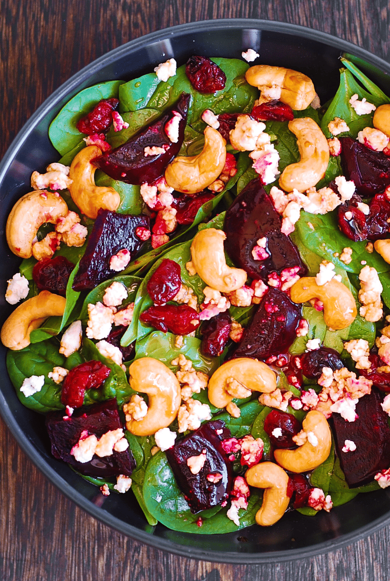 Beet Salad with Spinach, Cashews, Cranberries, and Goat Cheese - in a black bowl.