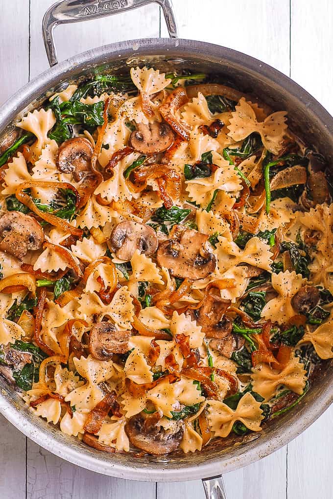 Creamy Bow-Tie Pasta with Spinach, Mushrooms, and Caramelized Onions - in a stainless steel pan.